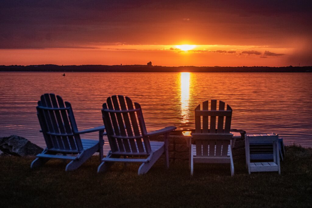 Three empty chairs facing a sunset over a lake.