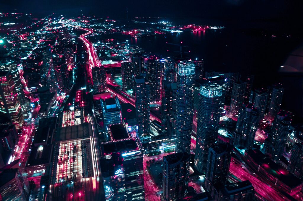 Aerial night view of a vibrant cityscape illuminated by pink and blue lights with busy streets.