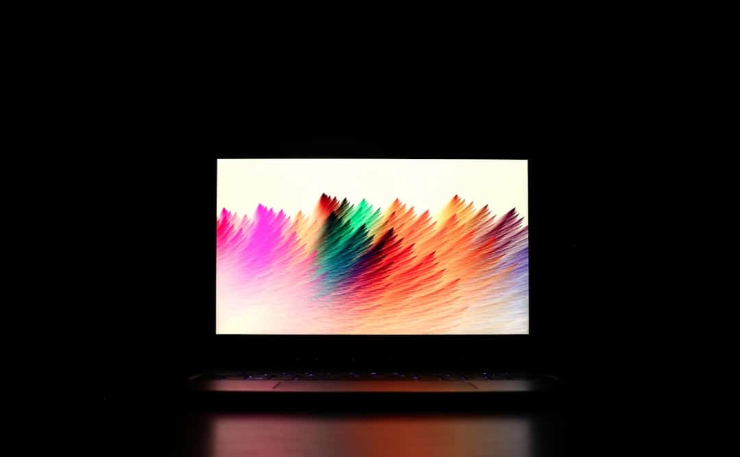 A laptop with a vibrant, abstract color pattern displayed on the screen, set against a dark background.