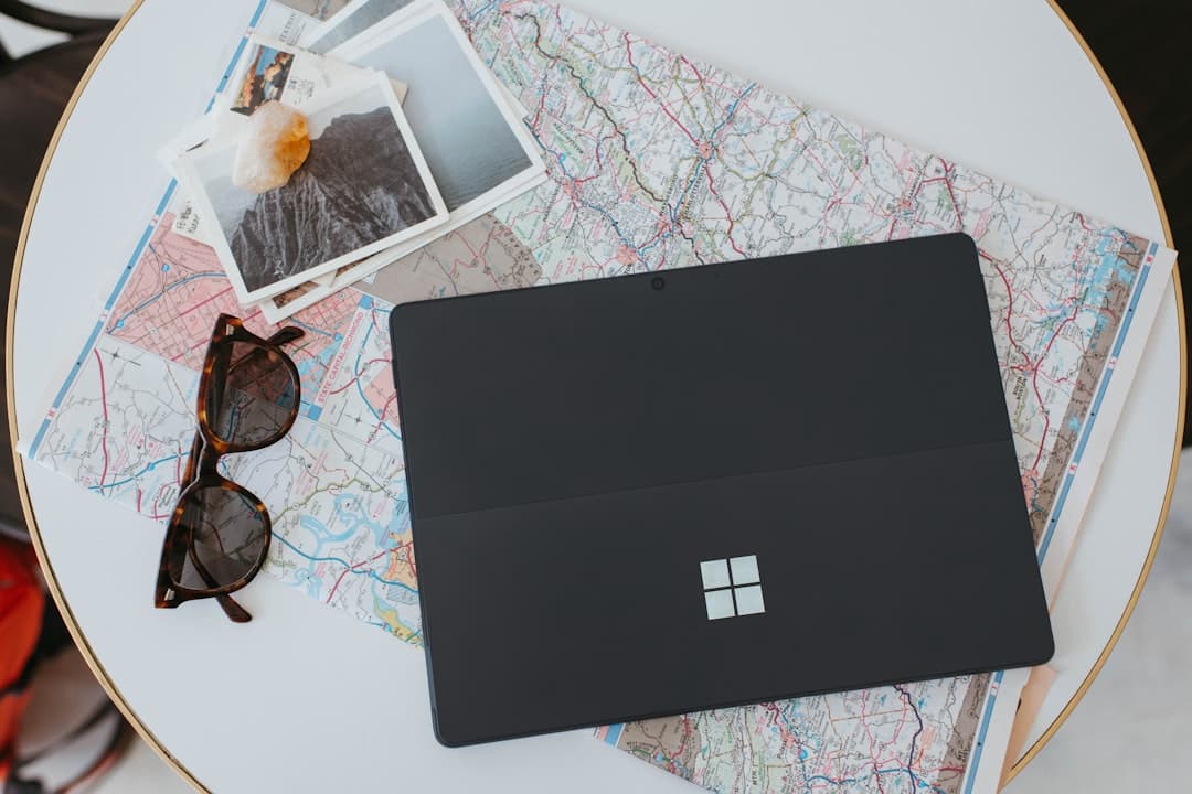 A laptop on top of a map, with sunglasses and several photographs adjacent.