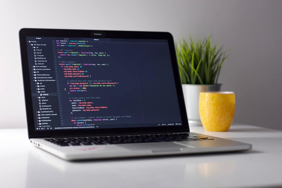 A laptop displaying code is on a desk. A yellow mug and a green plant are placed next to it.