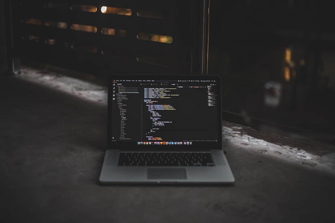 A laptop displaying code on a dark screen is open on a concrete surface, with dim lighting in the background.