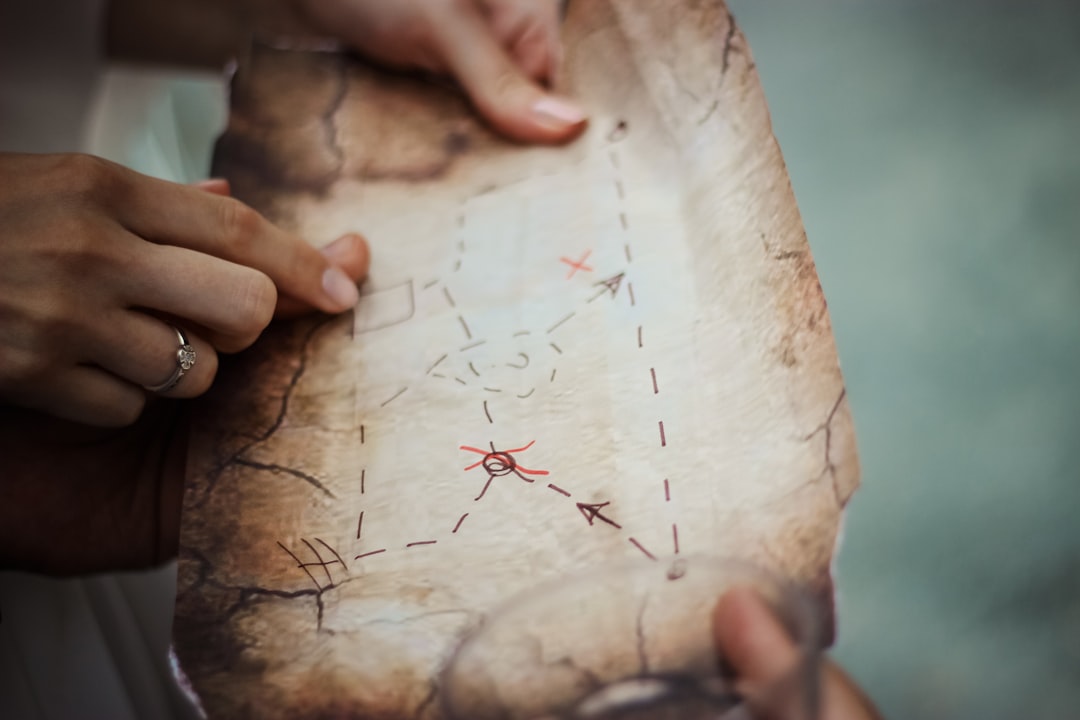 Hands holding an old, weathered treasure map with red X marks, arrows, and dotted paths.