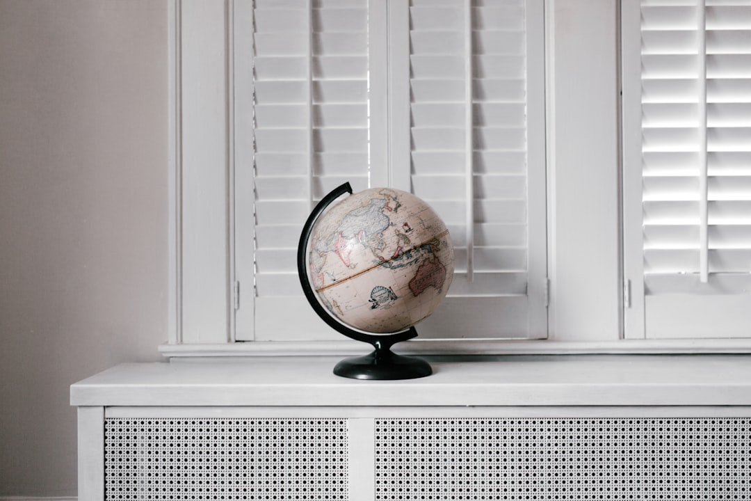 A vintage globe sits on a white radiator cover in front of white window shutters.