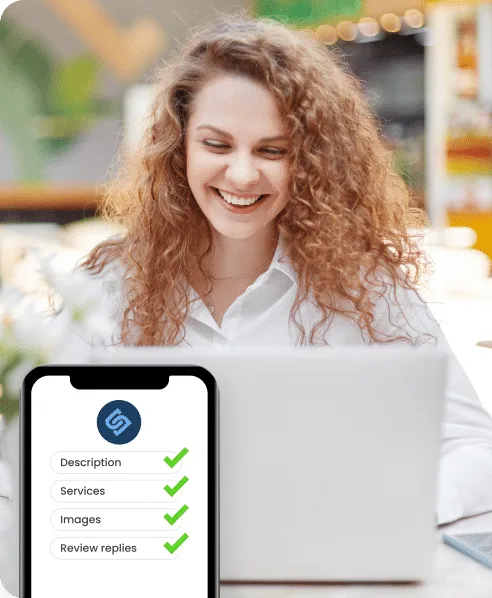 Smiling woman using a laptop with a smartphone displaying a checklist for Google Business Profile optimization, emphasizing services like description, images, and review replies.