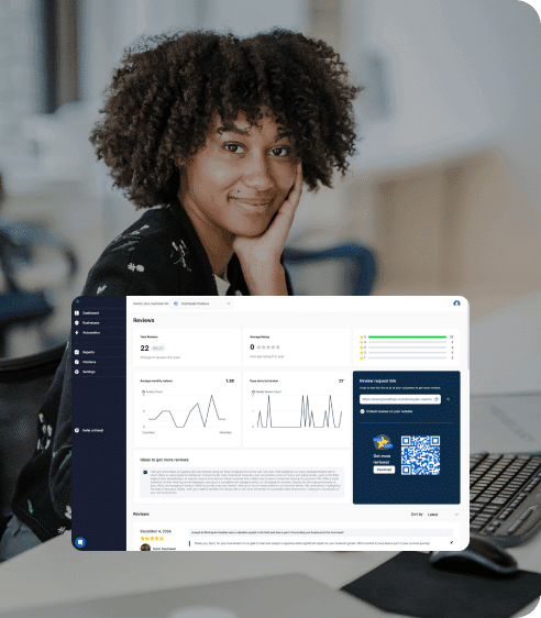 Woman smiling at camera, sitting at a desk with a laptop displaying analytics and graphs on the screen.