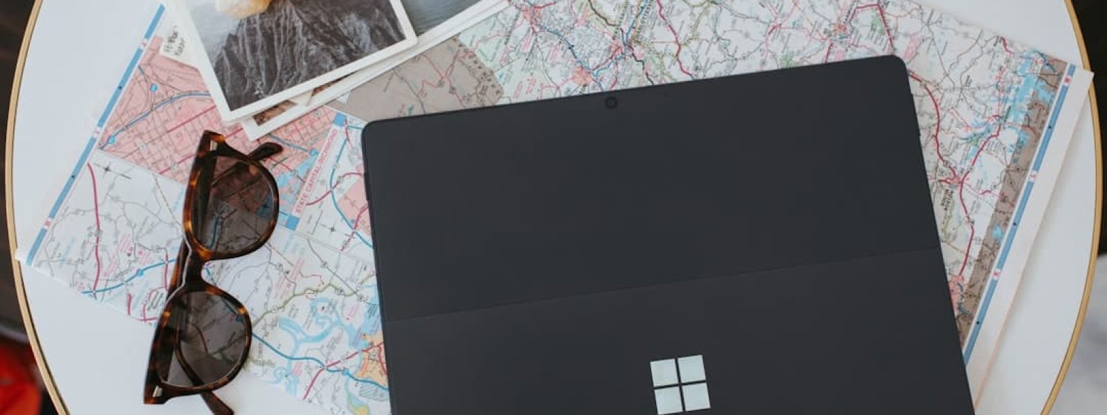 A laptop on top of a map, with sunglasses and several photographs adjacent.