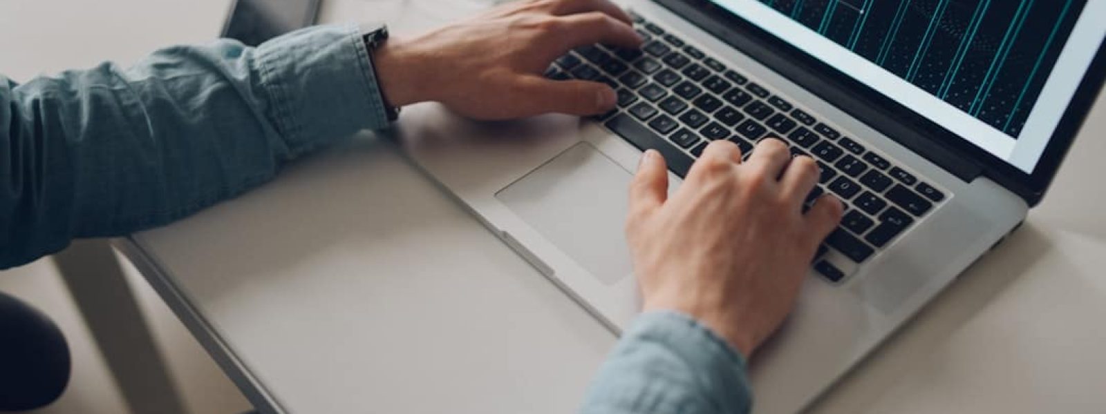 Person typing on a laptop at a desk with a smartphone, notepad, and earphones nearby.