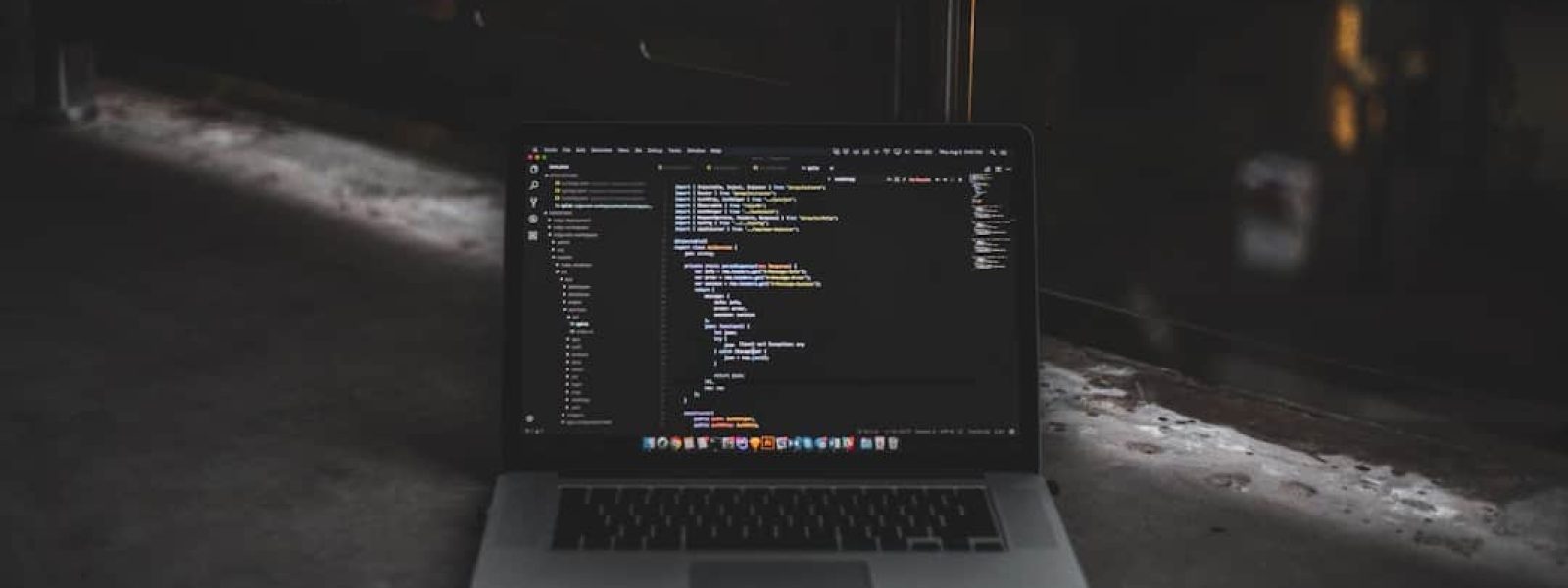 A laptop displaying code on a dark screen is open on a concrete surface, with dim lighting in the background.