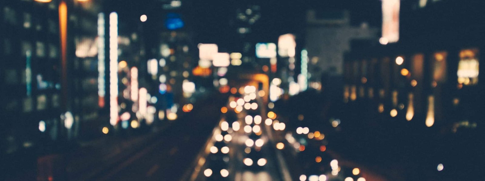 Blurred image of city street at night with illuminated buildings and moving car lights.