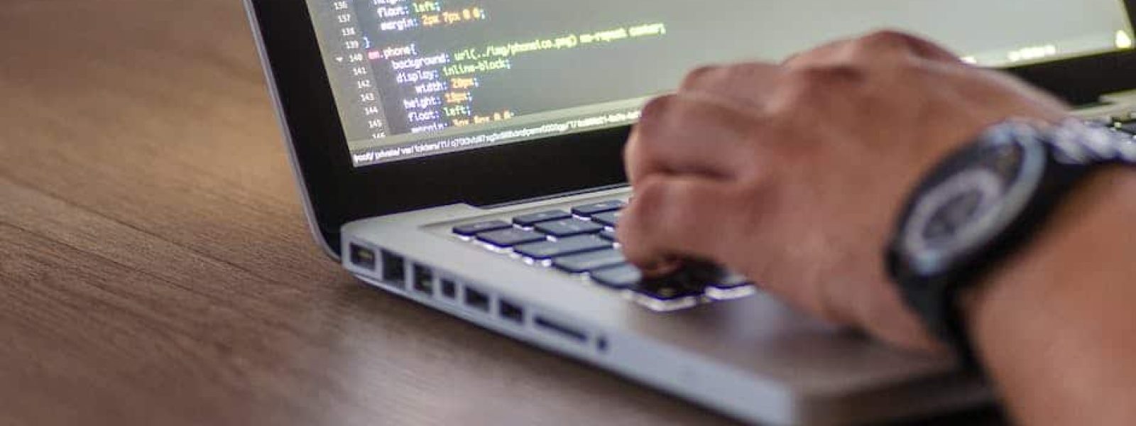 Person typing code on a laptop with a wooden table background.